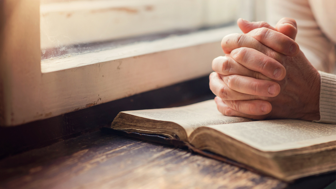 Hands of an unrecognizable woman with Bible praying