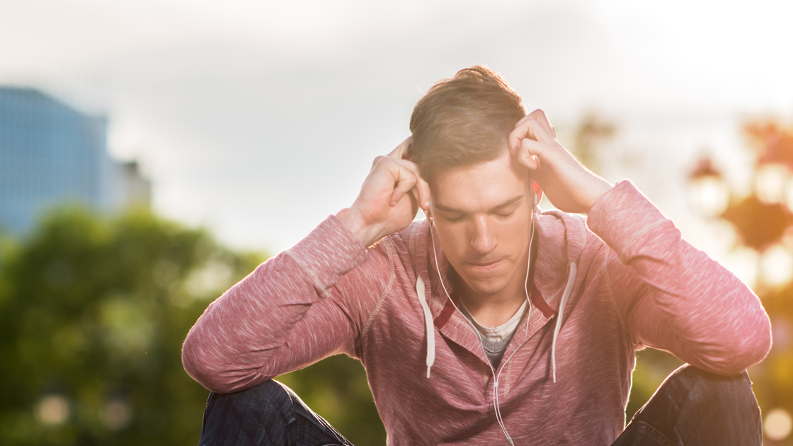 Stressed man holding his head in pain while trying to relax with music on MP3 player.