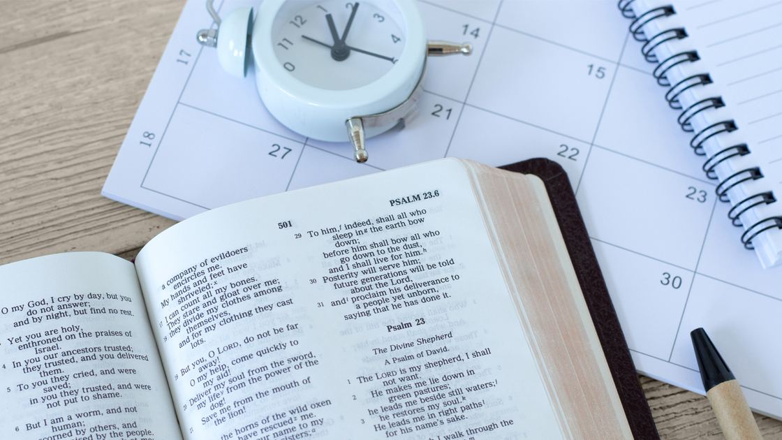Holy bible book with calendar, alarm clock and notebook on wooden table. Christian patience, study, and faith in God Jesus Christ, biblical concept.