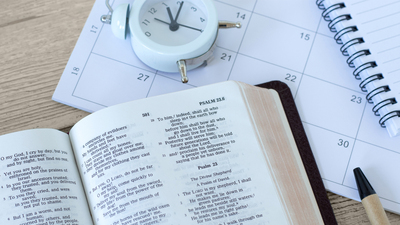 Holy bible book with calendar, alarm clock and notebook on wooden table. Christian patience, study, and faith in God Jesus Christ, biblical concept.