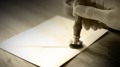 Elegant red wax seal stamp pressed onto a white envelope on a rustic wooden table.