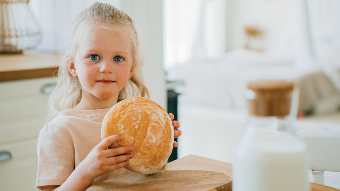 A lively moment as two sisters share laughter at a table, with a loaf of fresh bread creating a cheerful and inviting family kitchen scene.
