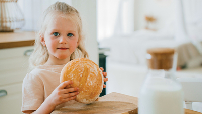 A lively moment as two sisters share laughter at a table, with a loaf of fresh bread creating a cheerful and inviting family kitchen scene.