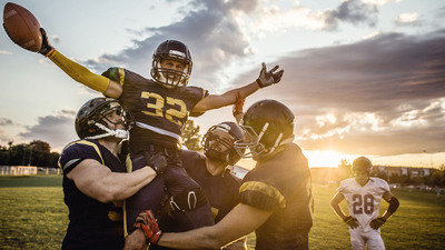 American football players holding their teammate high up on a playing field while celebrating a victory.