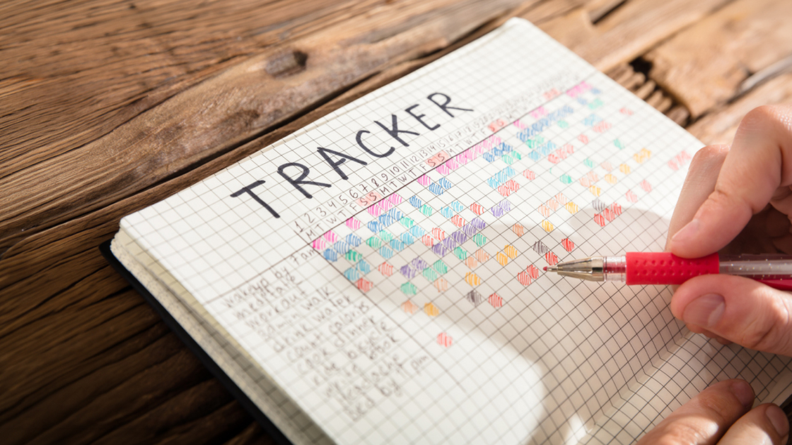 Close-up Of A Person's Hand Drawing Tracker Chart On Grid Notebook